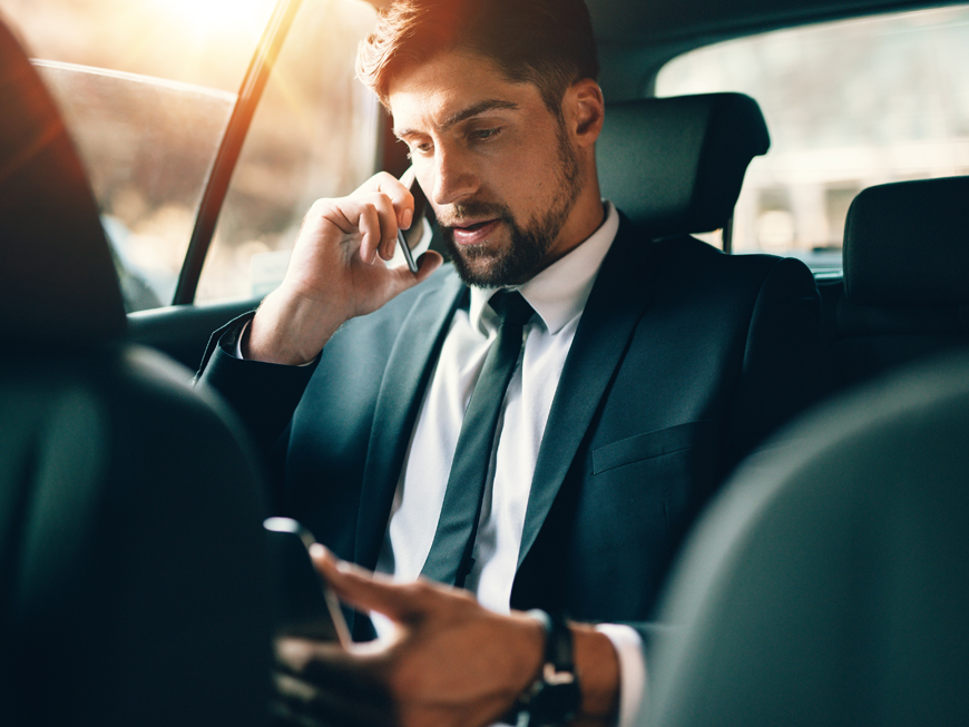 homme téléphonant à l'arrière d'un véhicule avec chauffeur pour illustrer le service pour les déplacements personnels ou professionnels